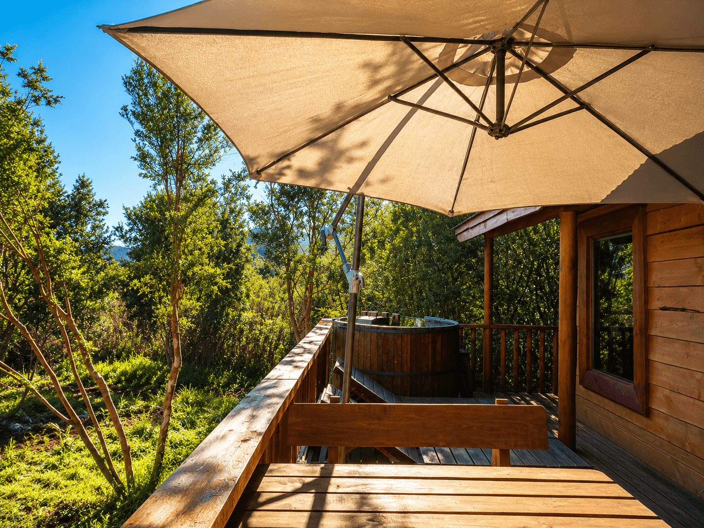 Terraza de la cabaña con tinaja de madera y quitasol, rodeada de vegetación