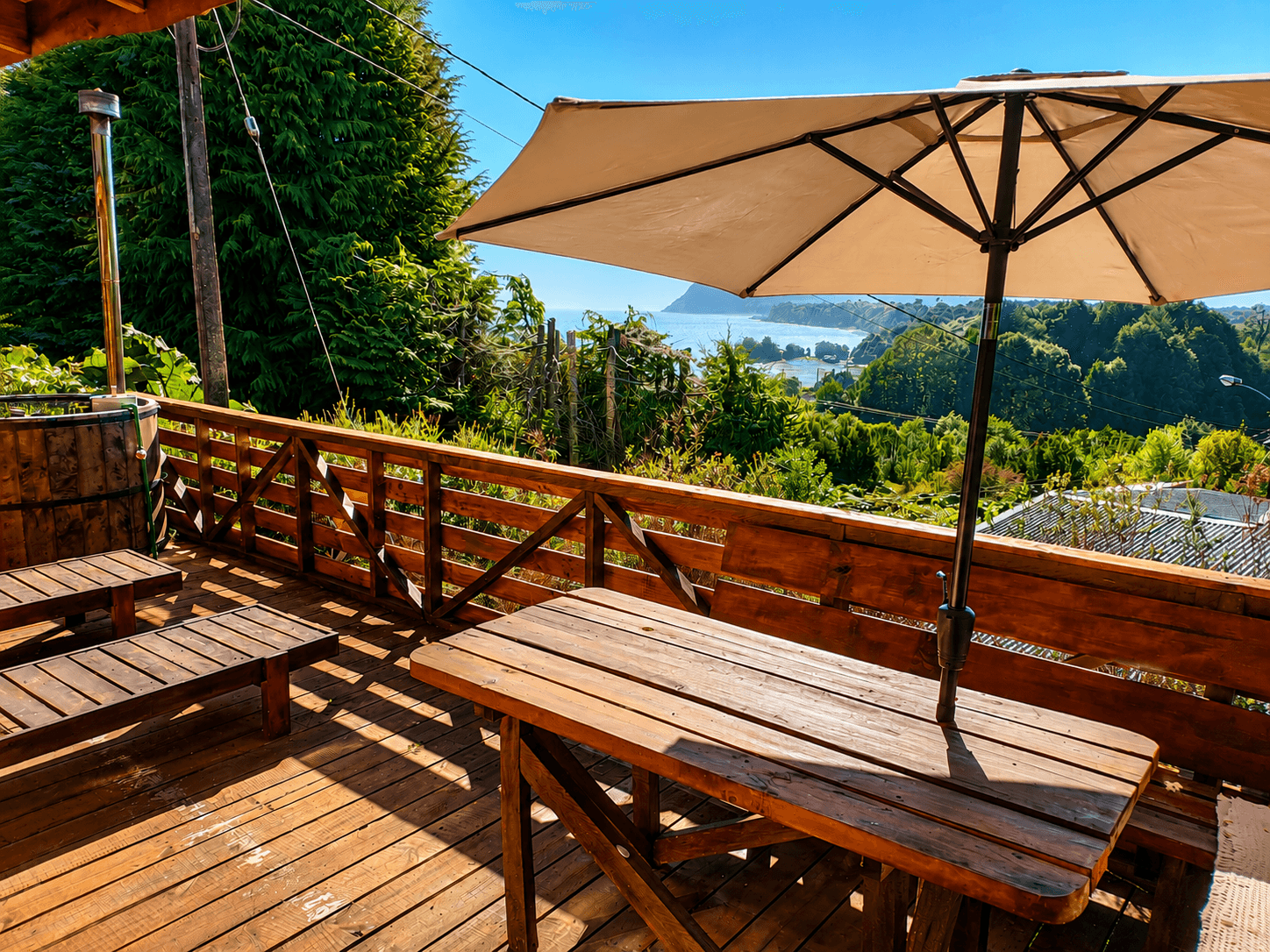 Terraza de la cabaña con quitasol, mesa de madera y vista a la bahía