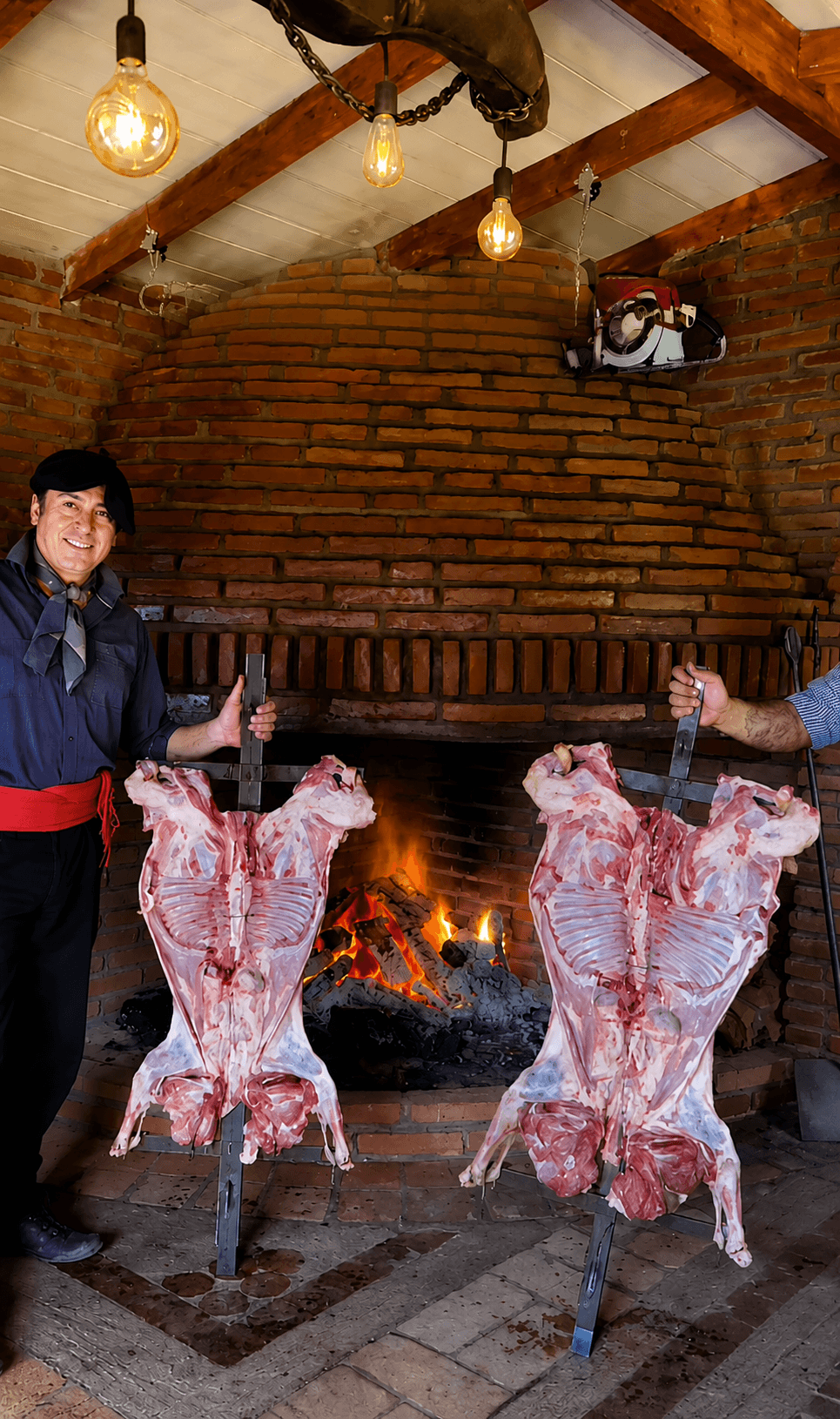 Corderos al palo abiertos en cruz frente al fogón de ladrillo, con el asador de boina y faja